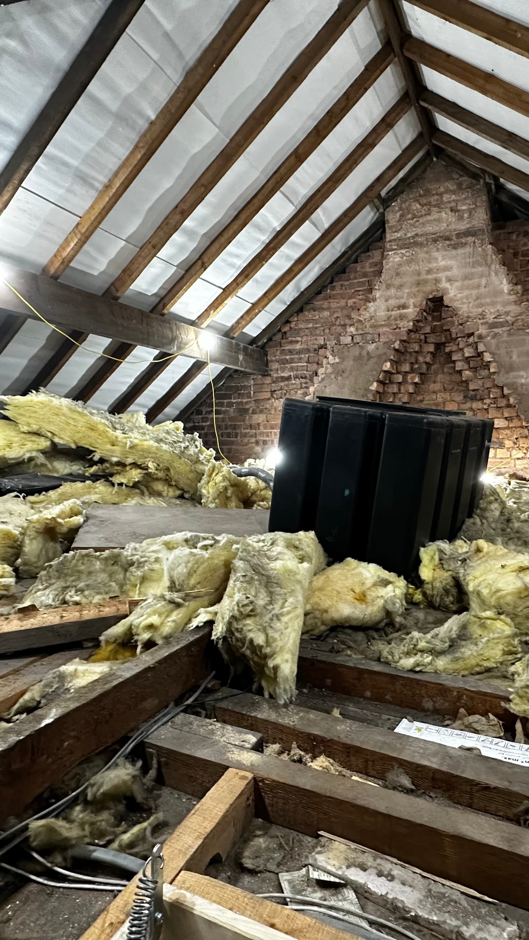 Attic space with wooden rafters, messy yellow insulation, and a large black water tank.