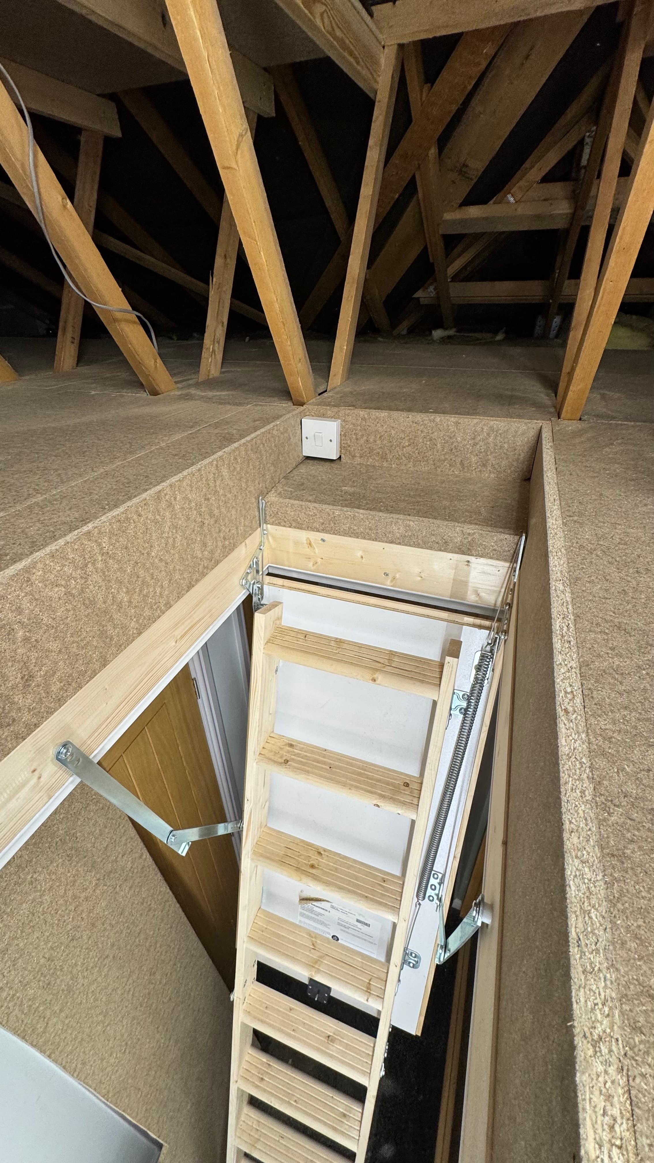 Wooden folding ladder leading down from a loft hatch in a chipboard floor.